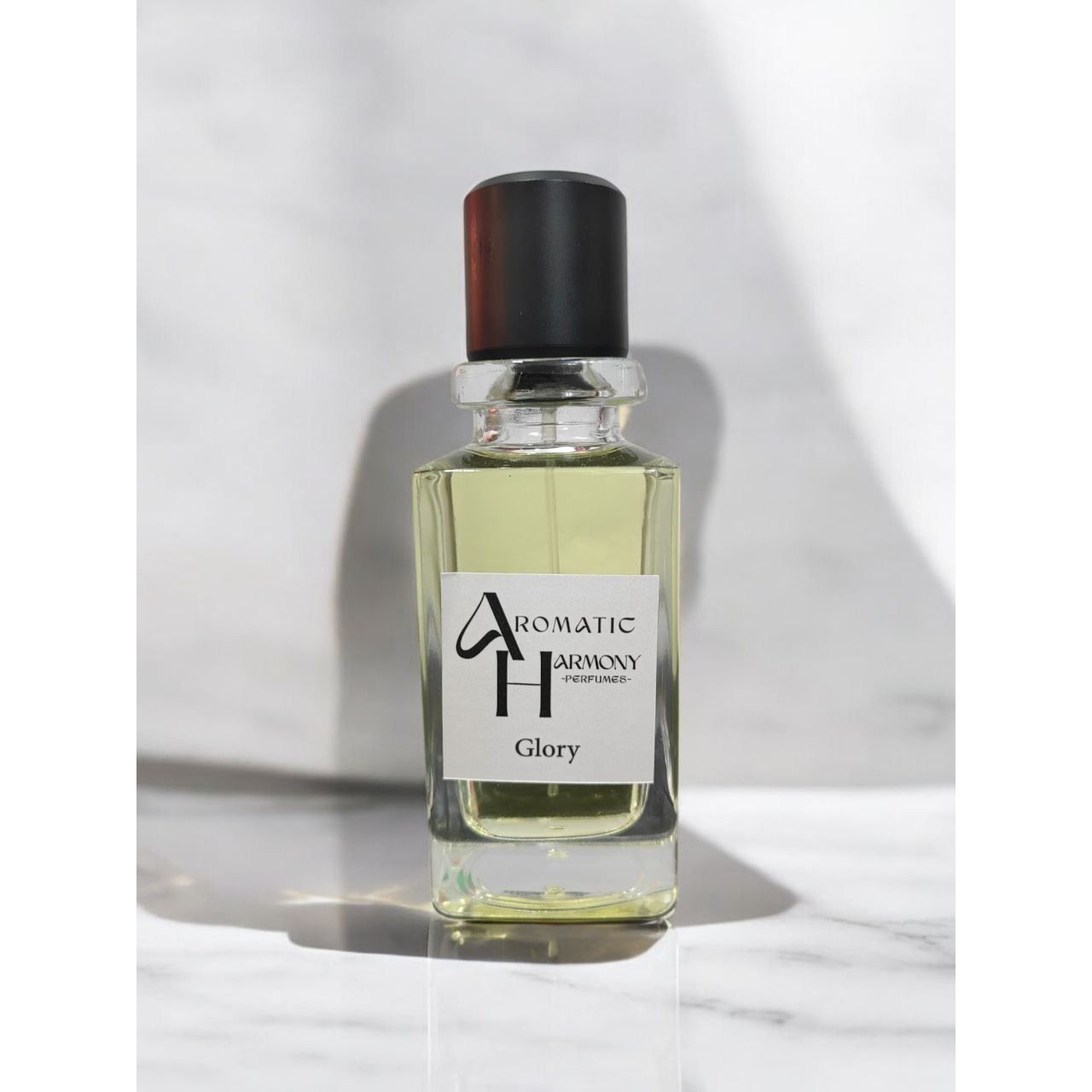 زجاجة عطر غلوري الشفافة بغطاء أسود وشعار متجر Aromatic Harmony